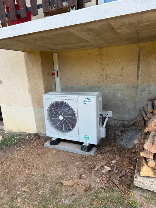 La même unité extérieure vue de l'autre côté, garde-corps en bois du balcon au-dessus, tas de bûches à droite