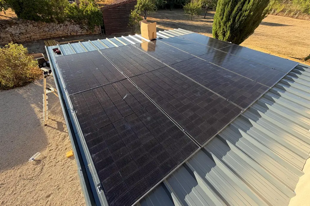 Panneaux photovoltaïques sur le bac acier gris d'une annexe, vus de dessus, mur de pierre, cabanon en bois et cyprès