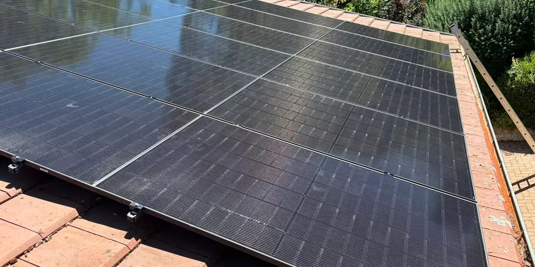 Trois rangées de panneaux photovoltaïques noirs sur une toiture en tuiles, jardin et haies en contrebas