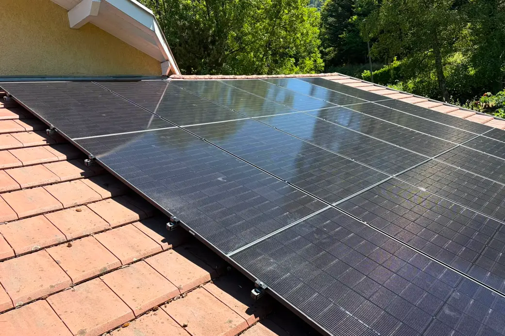 Panneaux photovoltaïques sur une toiture en tuiles rouges, pignon crépi jaune et forêt en arrière-plan