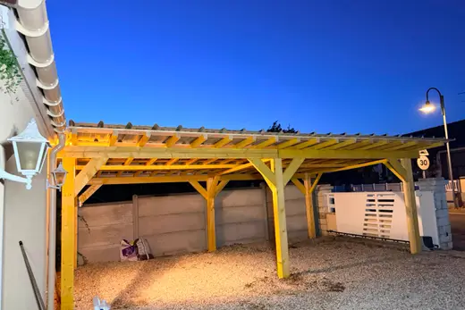 Le dessous du carport : poteaux, pannes et chevrons en bois, sous-face de la toiture en bac acier, sol en gravier