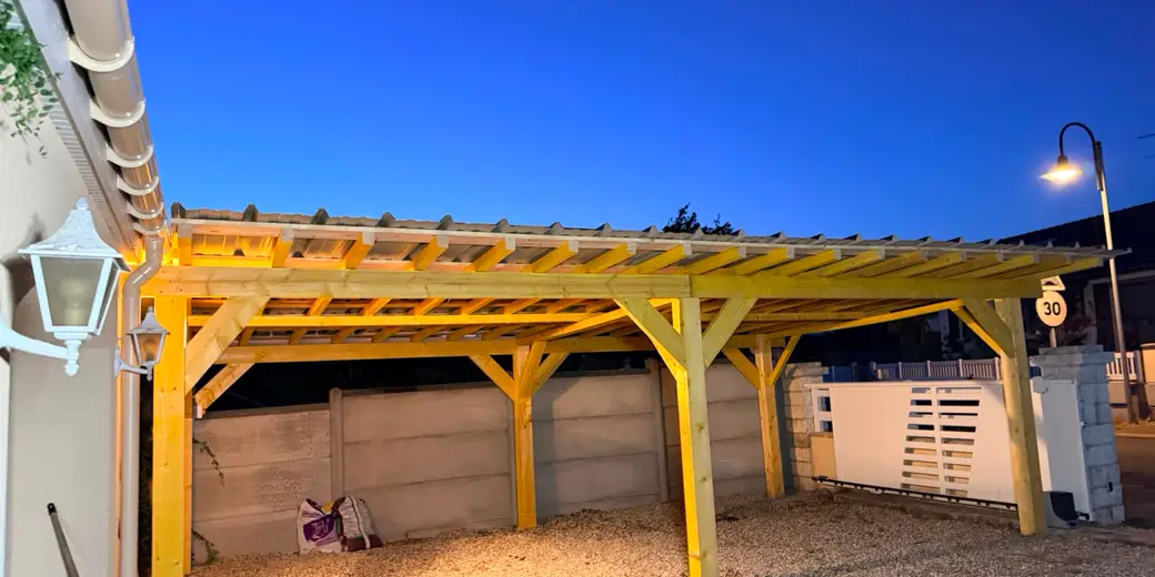Le dessous du carport : poteaux, pannes et chevrons en bois, sous-face de la toiture en bac acier, sol en gravier